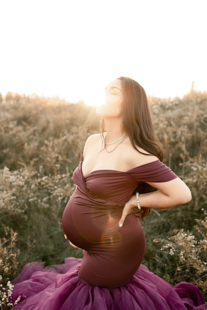 Pregnant mom with hand under belly in purple gown